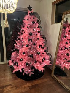 a pink christmas tree with black and white ornaments on it next to a large mirror