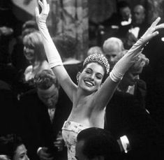 a black and white photo of a woman wearing a tiara with her arms in the air