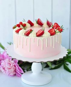 a strawberry cake with white icing and fresh strawberries on top, sitting next to pink flowers