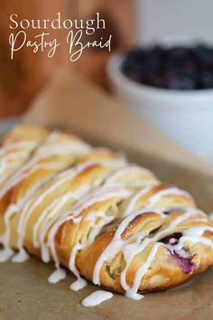 a pastry with white icing sitting on top of a counter next to a bowl of blueberries