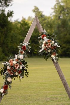 an arch decorated with flowers and greenery for a wedding ceremony in the middle of a field