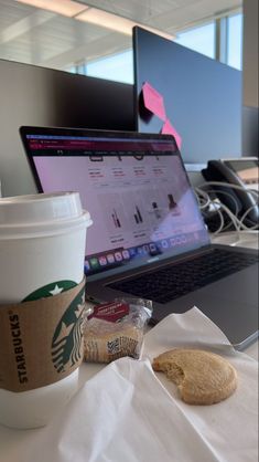 a cup of coffee next to a laptop on a table with a cookie and bag of chips