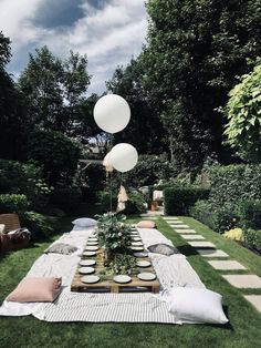 an outdoor table with balloons and plates on it in the middle of a lawn area