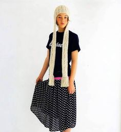 a woman wearing a hat and scarf standing in front of a white wall with polka dots