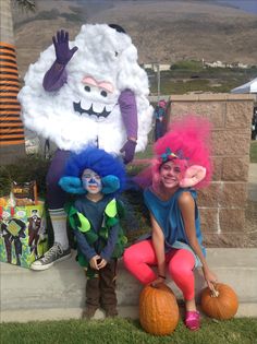 two children dressed in costumes sitting on pumpkins and posing for the camera with their faces painted