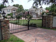 a gated driveway leading into a home with brick walkways and trees in the background