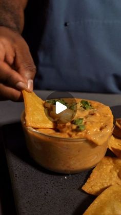 a person dipping some food into a bowl with tortilla chips on the side