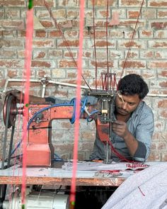 a man sitting at a table working on a sewing machine in front of a brick wall