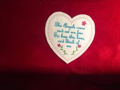 embroidered heart with words on it sitting on a red velvet surface in the shape of a flower