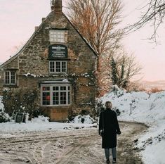 a person standing in front of a stone building with snow on the ground and trees