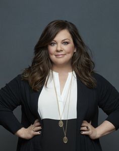 a woman standing in front of a gray background wearing a black and white top with her hands on her hips