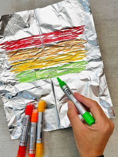 someone is drawing on foil with crayons and markers