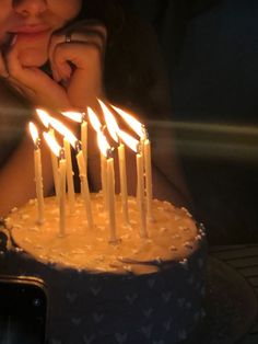 a woman sitting in front of a cake with lit candles