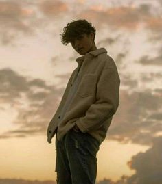 a young man standing on top of a roof with his hands in his pockets as the sun sets