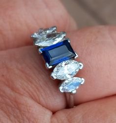 a woman's hand holding an engagement ring with blue and white stones