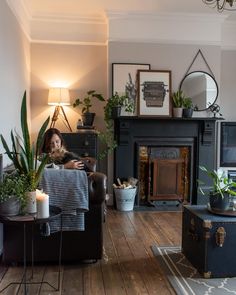 a woman sitting on a couch in front of a fire place with potted plants