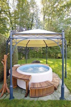 a hot tub in the middle of a yard with a gazebo and wooden benches