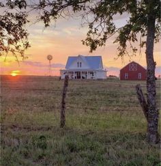 the sun sets over a farm with a red barn in the foreground