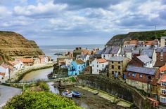 boats are parked on the shore in front of some buildings and cliffs near the ocean