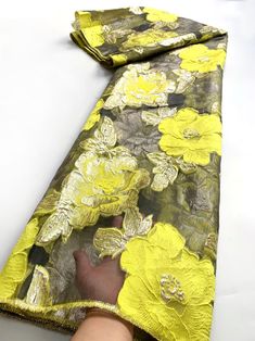 a person is holding onto a yellow and black flowered scarf on a white surface