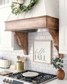 a kitchen with white cabinets and a wooden shelf above the stove top that says hello fall