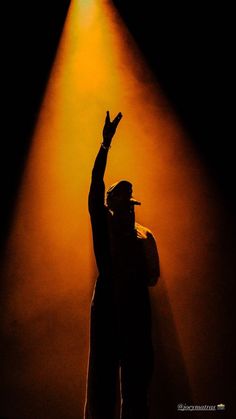 a man standing in front of a spotlight on stage with his hand up to the sky