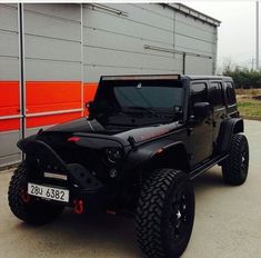 a black jeep is parked in front of a building with an orange stripe on it