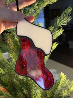 a hand holding a christmas stocking ornament in front of a pine tree