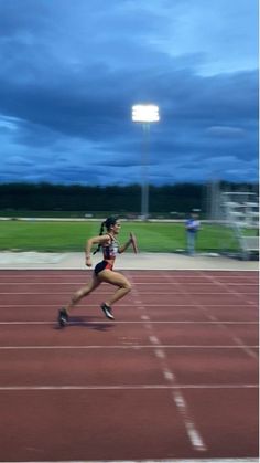 a woman is running on a track at night with the sky in the back ground