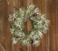 a christmas wreath is hanging on a wooden fence with pine cones and snow flakes