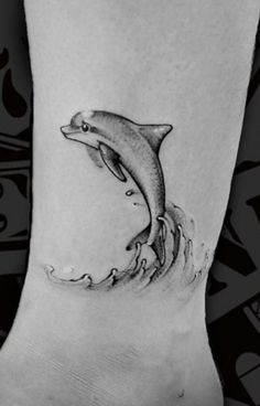 a dolphin tattoo on the ankle with water splashing from it's mouth and feet