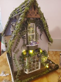 a doll house with plants growing on the roof and windows in it's corner