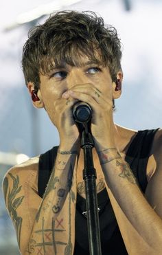 a man with tattoos on his arms holding a microphone in front of his face as he sings