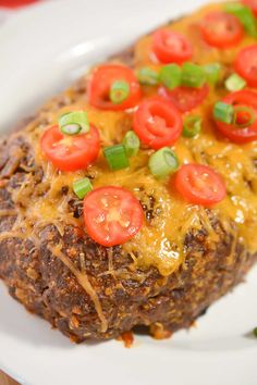 a close up of a plate of food with cheese and tomatoes on top, along with green onions