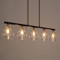 five clear glass globes are hanging from a long black metal bar light fixture with gold fittings