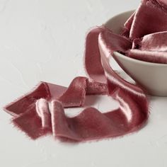 a white bowl filled with pink satin ribbon next to a red napkin on top of a table