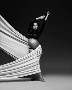 a pregnant woman wrapped in white fabric posing for a magazine cover photo shoot with her belly exposed