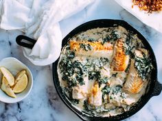 a skillet filled with chicken and spinach covered in gravy next to sliced lemons