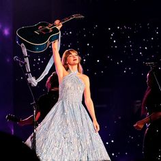 a woman in a blue dress holding up a guitar