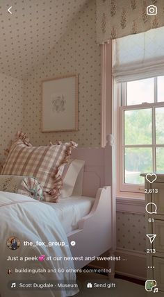 a bed sitting under a window next to a wallpaper covered in pink and white