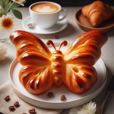 a cake shaped like a butterfly sitting on top of a plate next to a cup of coffee