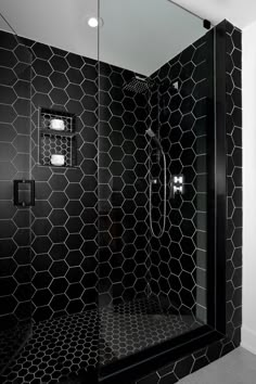 a black and white bathroom with hexagonal tiles on the shower wall, toiletries in the corner