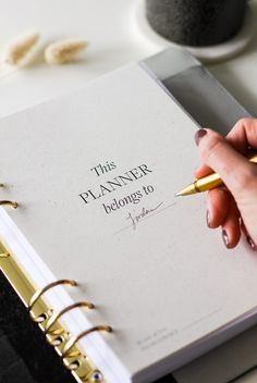 a woman's hand holding a pen and writing on a planner