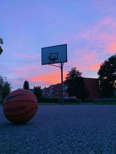 a basketball is sitting on the ground in front of a basket ball at sunset or dawn