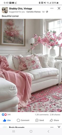 a living room with white furniture and pink flowers on the couch, in front of a window