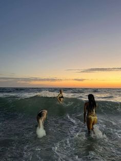 three people in the ocean at sunset with one person on a surfboard and two others running into the water