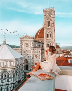 a woman sitting on top of a roof next to a building with a pizza in front of her