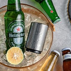 two bottles of heineken are sitting in an ice bucket with some lemons