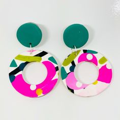 a pair of colorful earrings on a white surface with green and pink circulars in the middle