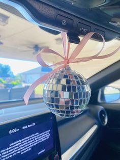 a disco ball hanging from the dashboard of a car with a pink ribbon around it